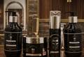 Set of hair care products on a wooden surface with a mirror and grooming tools in the background.